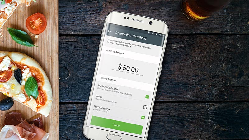 A flatlay of a pizza and a mobile phone showing a transaction threshold of $50 on the screen. A flatlay of a pizza and a mobile phone showing a transaction threshold of $50 on the screen.
