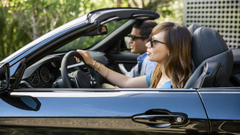 A woman driving a black convertible car and a man in the passenger seat. A woman driving a black convertible car and a man in the passenger seat.